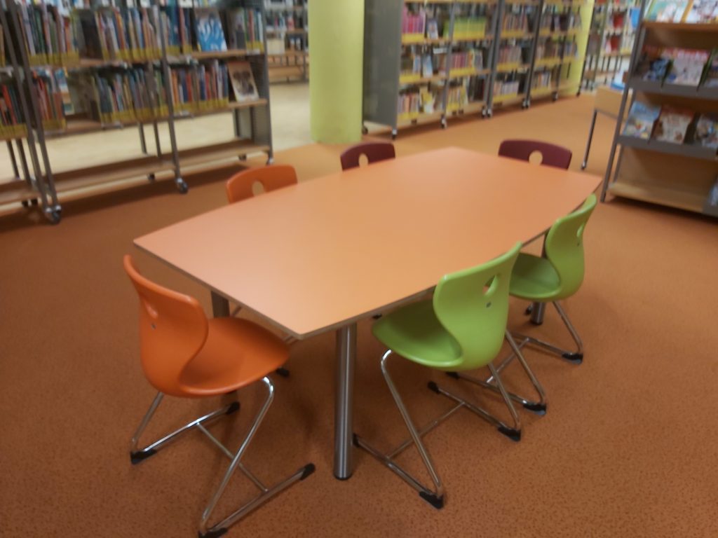 Foto zeigt einen Tisch in der Stadtbibliothek Siegen, an dem Kinder und Erwachsene sitzen können.
