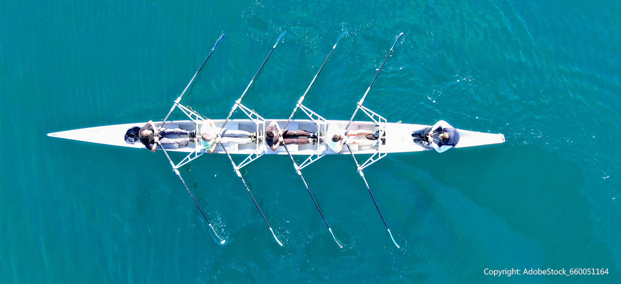 Vier Personen rudern in einem Ruderboot mit Steuermann